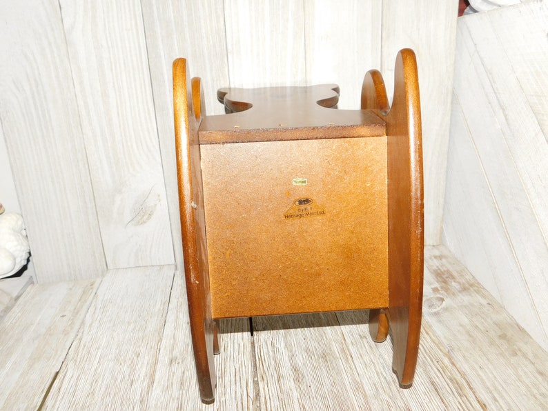 Puede incluir: Una silla mecedora de madera con un peque&ntilde;o estante en la parte posterior. La silla est&aacute; hecha de madera marr&oacute;n claro y tiene un dise&ntilde;o sencillo. El estante tiene una etiqueta que dice "Early American Heritage Woodcraft".