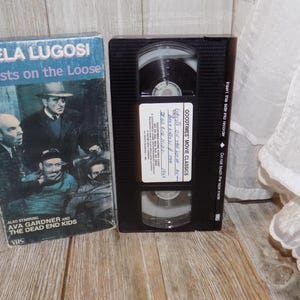 May include: A vintage VHS tape and box set. The box features the title "Ghosts on the Loose" with Bela Lugosi's name and a movie poster. The black VHS tape has a label with the movie title and Goodtimes Movie Classics.
