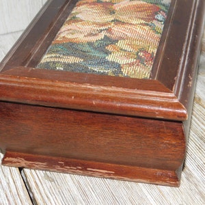 May include: A wooden box with a floral tapestry lid. The box is dark brown and has a slightly rounded shape. The lid is slightly raised and has a decorative border.