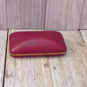 May include: A red leather glasses case with gold trim. The case has the word "SACHIN" embossed on the top.