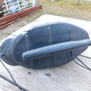 May include: Black plastic decoy of a duck with a black cord attached to the bottom. The decoy has a textured surface and a small black handle on the back.