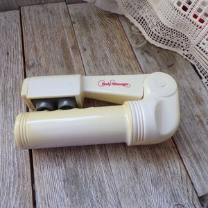May include: A white handheld body massager with three rolling balls and a red "Body Massager" label.