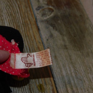 May include: A red and white polka dot fabric doll with a black fabric head and a brown tag that reads "applause. APPLAUSE INC. WOODLAND HILLS MADE IN CHINA THE WALT DIS REG. NO. P.A. 4 CONTENTS: ALL N ITEM NO. 8535"