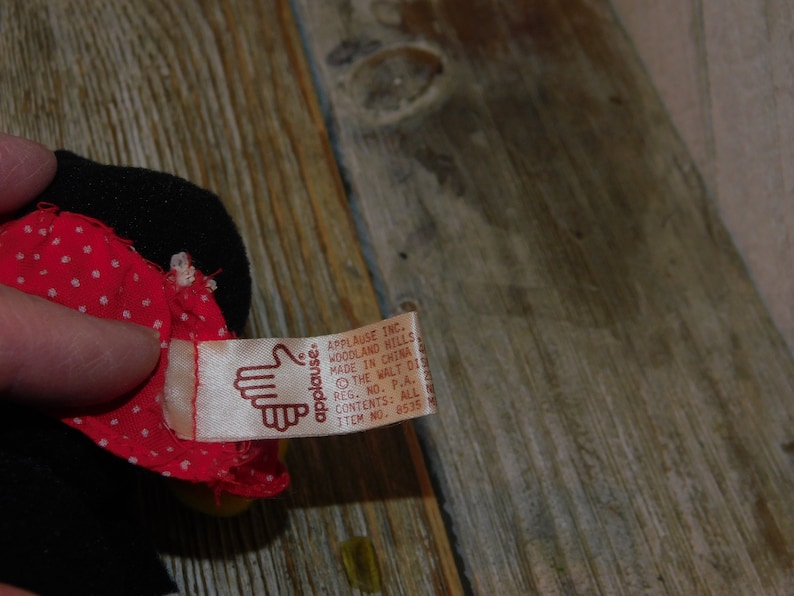 May include: A red and white polka dot fabric doll with a black fabric head and a brown tag that reads "applause. APPLAUSE INC. WOODLAND HILLS MADE IN CHINA THE WALT DIS REG. NO. P.A. 4 CONTENTS: ALL N ITEM NO. 8535"