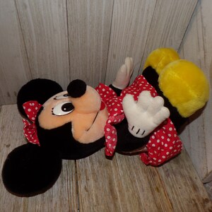 K&ouml;nnte beinhalten: Ein Pl&uuml;schtier von Minnie Mouse, das ein rotes Kleid mit wei&szlig;en Punkten und eine rote Schleife mit wei&szlig;en Punkten tr&auml;gt. Das Spielzeug hat schwarze Ohren und einen gelben K&ouml;rper.