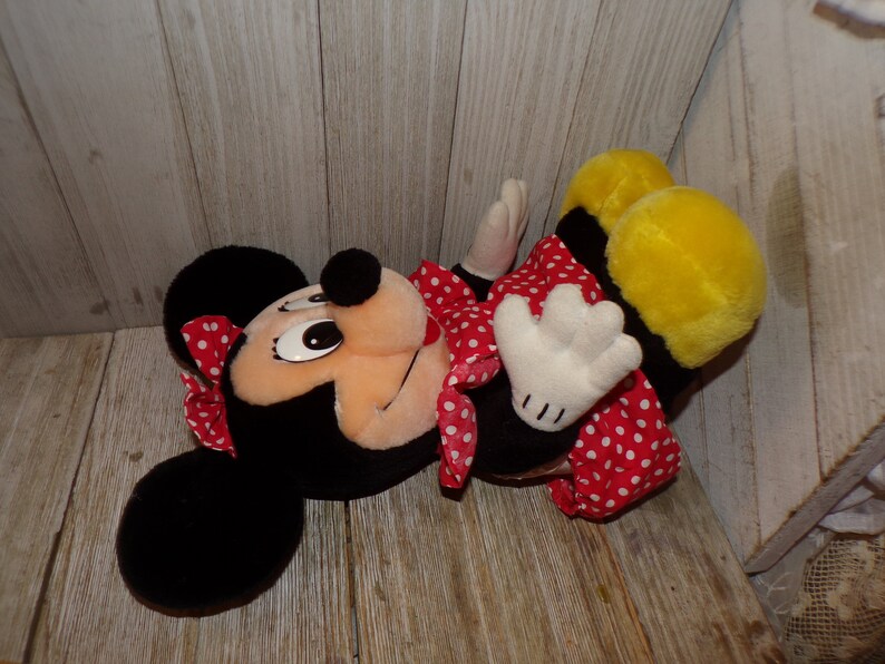 K&ouml;nnte beinhalten: Ein Pl&uuml;schtier von Minnie Mouse, das ein rotes Kleid mit wei&szlig;en Punkten und eine rote Schleife mit wei&szlig;en Punkten tr&auml;gt. Das Spielzeug hat schwarze Ohren und einen gelben K&ouml;rper.
