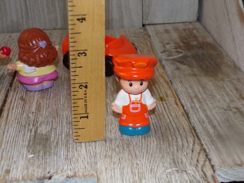 May include: A set of three plastic figurines, including a girl with brown hair wearing a yellow shirt and pink trousers, a boy wearing a red hat and overalls, and a red car. The figurines are approximately 5 cm tall.