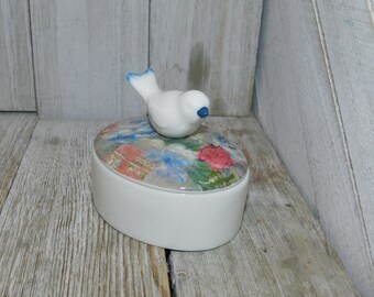 May include: White ceramic trinket box with a floral design on the lid. A white bird with blue accents sits on top of the lid.