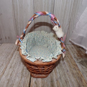 Peut inclure: Un petit panier en osier avec une poign&eacute;e en ruban bleu et rose. Le panier est doubl&eacute; d'un tissu floral et a un lapin en peluche blanc attach&eacute; &agrave; la poign&eacute;e.
