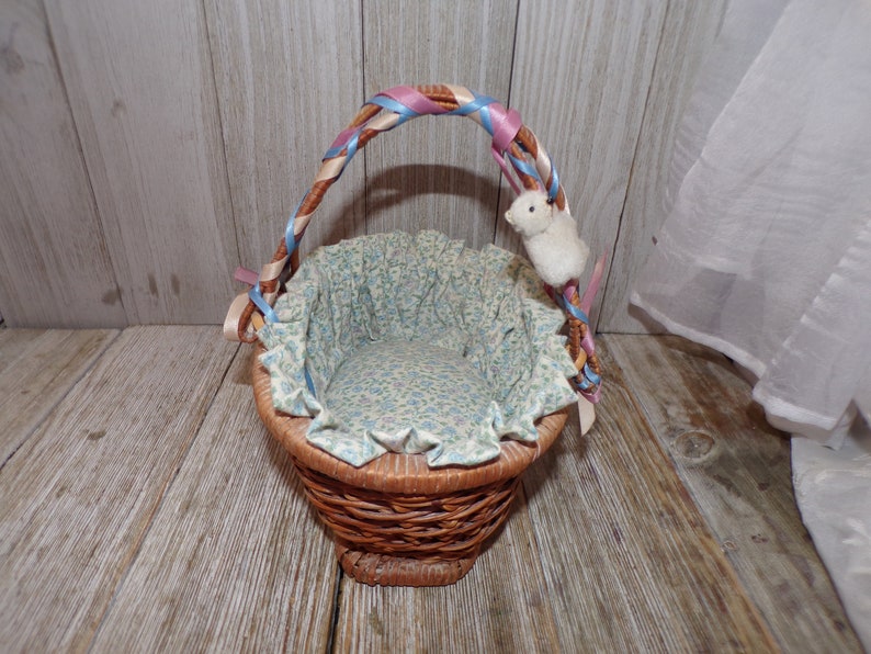 Peut inclure: Un petit panier en osier avec une poign&eacute;e en ruban bleu et rose. Le panier est doubl&eacute; d'un tissu floral et a un lapin en peluche blanc attach&eacute; &agrave; la poign&eacute;e.