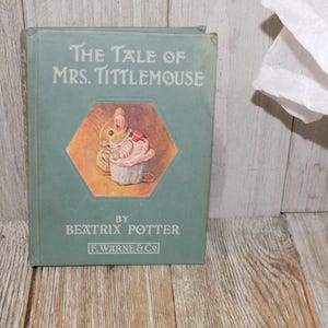 May include: A vintage copy of "The Tale of Mrs. Tittlemouse" by Beatrix Potter. The book has a teal cover with the title in white lettering and a colorful illustration of a mouse and a cupcake. Published by F. Warne & Co.