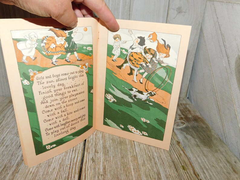Op de afbeelding: Een open boek met kleurrijke illustraties van kinderen die buiten spelen. De tekst op de pagina luidt: "Girls and boys come out to play The sun shines bright this lovely day Finish your breakfast of good things to eat... And join your playmates down on the street Come with a hoop and come with a ball. Come with a kite and come with a doll. Come with laughter merry and gay To play out of doors this livelong day"