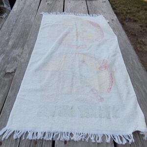 Peut inclure: Serviette rectangulaire blanche avec un motif color&eacute;. La serviette a un bord &agrave; franges et semble &ecirc;tre faite d'un mat&eacute;riau doux et absorbant. Le motif pr&eacute;sente des &eacute;l&eacute;ments rouges, jaunes et bleus. La serviette est pos&eacute;e sur une surface en bois vieilli.