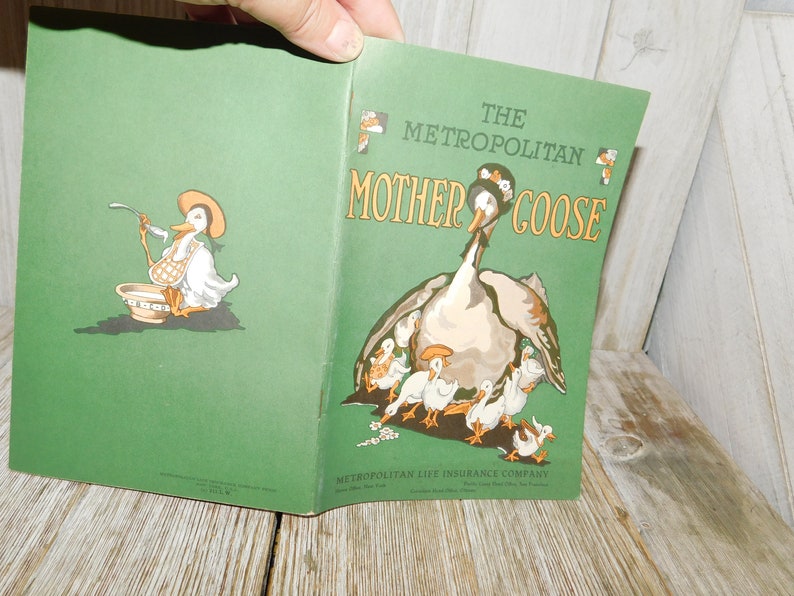 Op de afbeelding: Een vintage groen boek getiteld "The Metropolitan Mother Goose" met een illustratie van een moedergans en haar gansjes op de omslag. De Metropolitan Life Insurance Company staat afgedrukt onderaan de omslag.