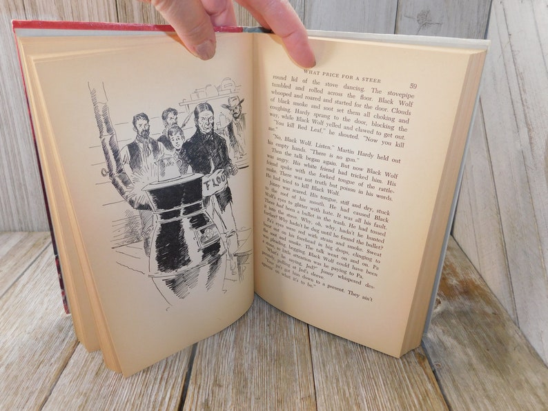 May include: A black and white illustration of a group of people standing around a large metal stove with a sign that reads "Flour". The illustration is from a book titled "What Price for a Steer".