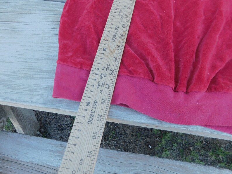 May include: A close-up of the bottom edge of a red velvet garment. A wooden ruler is visible with markings in inches and centimeters. The ruler reads "461-3800" and "2301 So. 300 W. So. Salt Lake".