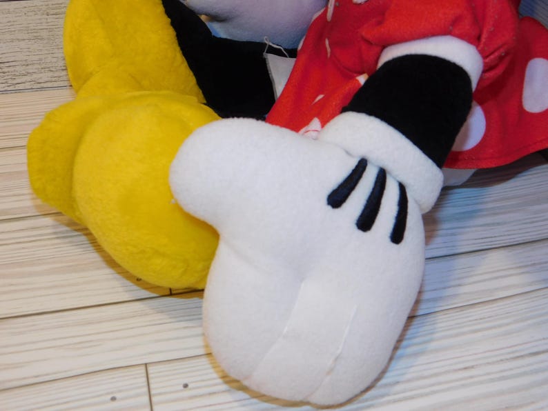 Op de afbeelding: Close-up van een pluche speelgoed met een witte handschoen met zwarte details, een gele voet en een rode mouw met stippen. Het speelgoed is waarschijnlijk een personage uit een populaire tekenfilm.