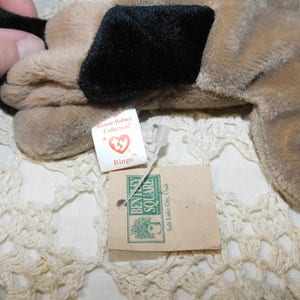 K&ouml;nnte beinhalten: Ein braunes und schwarzes Pl&uuml;schtierhund namens "Ringo" aus der Beanie Babies Collection. Das Spielzeug ist an einem wei&szlig;en Etikett mit dem Ty-Logo und den Worten "Beanie Babies Collection" und "Ringo" befestigt. Das Etikett ist an einem braunen Papieretikett mit den Worten "Beanie Square" und "Salt Lake City, Utah" befestigt.