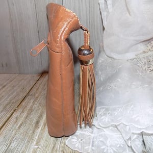 May include: A brown leather purse with a zipper closure and a tassel. The purse has a quilted design and a gold-toned zipper pull.