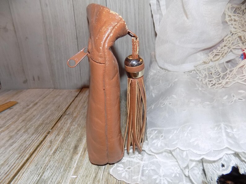 May include: A brown leather purse with a zipper closure and a tassel. The purse has a quilted design and a gold-toned zipper pull.