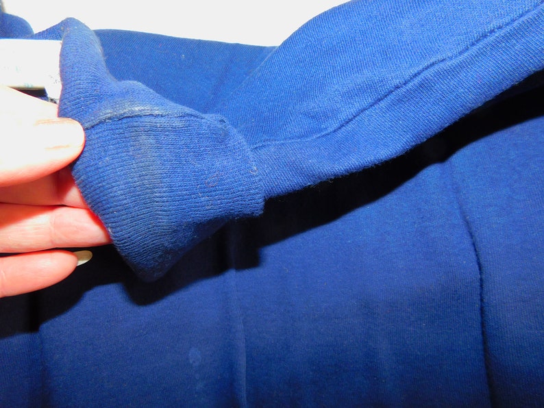 May include: Close-up of the blue fabric cuff of a long-sleeved shirt. The fabric is soft and has a slight texture.