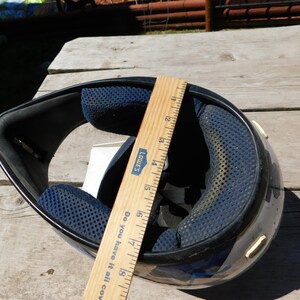 May include: Black and blue motorcycle helmet with a blue and white graphic design. The helmet is being measured with a wooden ruler that reads "Lowe's" and "Do you have it all covered?" The ruler measures 18 inches.