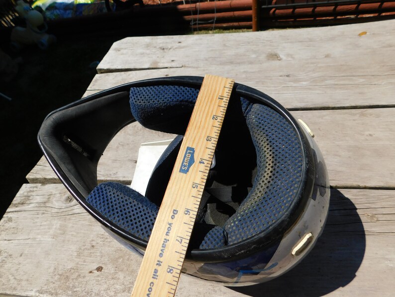 May include: Black and blue motorcycle helmet with a blue and white graphic design. The helmet is being measured with a wooden ruler that reads "Lowe's" and "Do you have it all covered?" The ruler measures 18 inches.