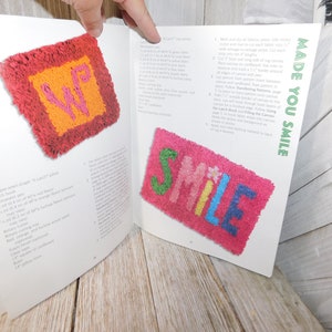 May include: A book titled "Make Your Own" with the words "Made You Smile" on the cover. The book features instructions for creating latch hook rugs. The book shows two examples of latch hook rugs, one with the letters "WP" and the other with the word "SMILE".