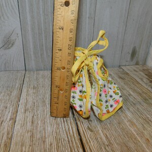 May include: A yellow and white floral print doll dress with a yellow ribbon tie. The dress has a pink and yellow trim.