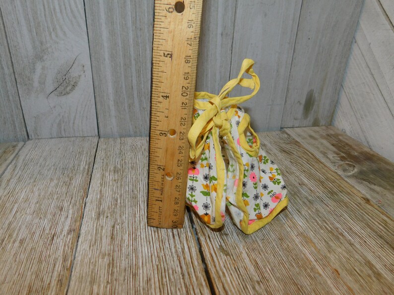 May include: A yellow and white floral print doll dress with a yellow ribbon tie. The dress has a pink and yellow trim.