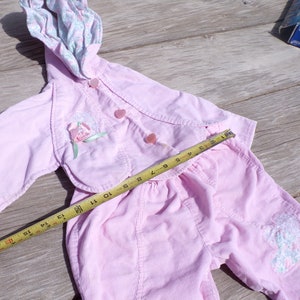 Puede incluir: Un conjunto de beb&eacute; de pana rosa con una chaqueta con capucha y pantalones. La chaqueta tiene un dise&ntilde;o floral y botones. Los pantalones tienen un dise&ntilde;o floral en una pierna. Una cinta m&eacute;trica se coloca sobre el conjunto.