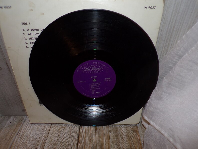 Puede incluir: Un disco de vinilo negro con una etiqueta morada que dice "Alshire Presents All Strings" y "Jet Set" con una lista de canciones. El n&uacute;mero del disco es W 9037.