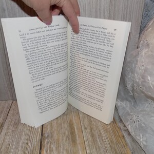May include: Open book with white pages and black text. The book is titled "Games and Fun with Playing Cards". The text describes different card games, including "Donkey" and "14 Cards for Three or Four Players".