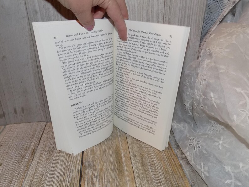 May include: Open book with white pages and black text. The book is titled "Games and Fun with Playing Cards". The text describes different card games, including "Donkey" and "14 Cards for Three or Four Players".