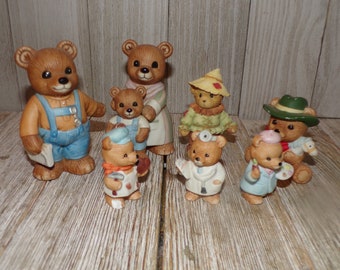 May include: A collection of eight brown teddy bear figurines, each dressed in a different costume. The bears are wearing outfits like a doctor, a painter, a farmer, and a construction worker.