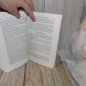May include: Open book with white pages and black text. The book is titled "Games and Fun with Playing Cards". The text on the left page discusses a card game called "Cards and Fun with Playing Cards". The text on the right page discusses a card game called "Seven-Card Stud Poker".