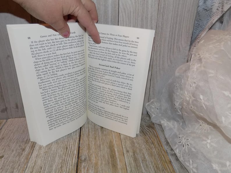 May include: Open book with white pages and black text. The book is titled "Games and Fun with Playing Cards". The text on the left page discusses a card game called "Cards and Fun with Playing Cards". The text on the right page discusses a card game called "Seven-Card Stud Poker".