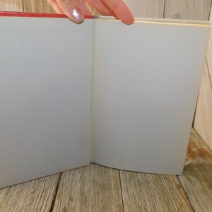 May include: An open book with a red cover and blank white pages. The book is lying open on a wooden surface.