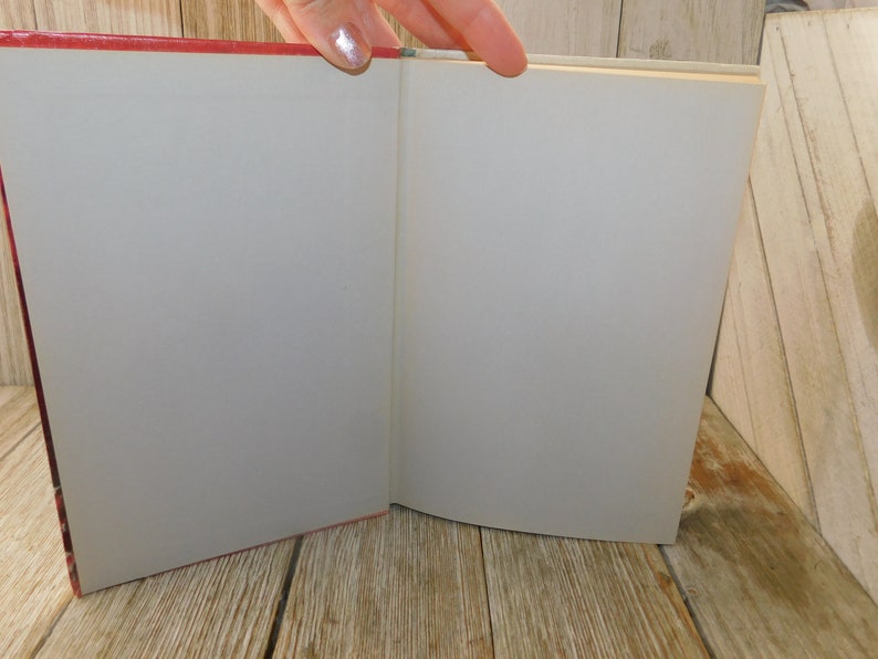 May include: An open book with a red cover and blank white pages. The book is lying open on a wooden surface.