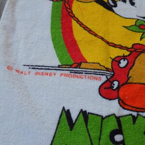 Peut inclure: Serviette blanche avec un motif Mickey Mouse color&eacute;. Le motif comprend Mickey Mouse, un fond rouge et jaune, et le texte "Mickey". La serviette porte &eacute;galement le texte "WALT DISNEY PRODUCTIONS".