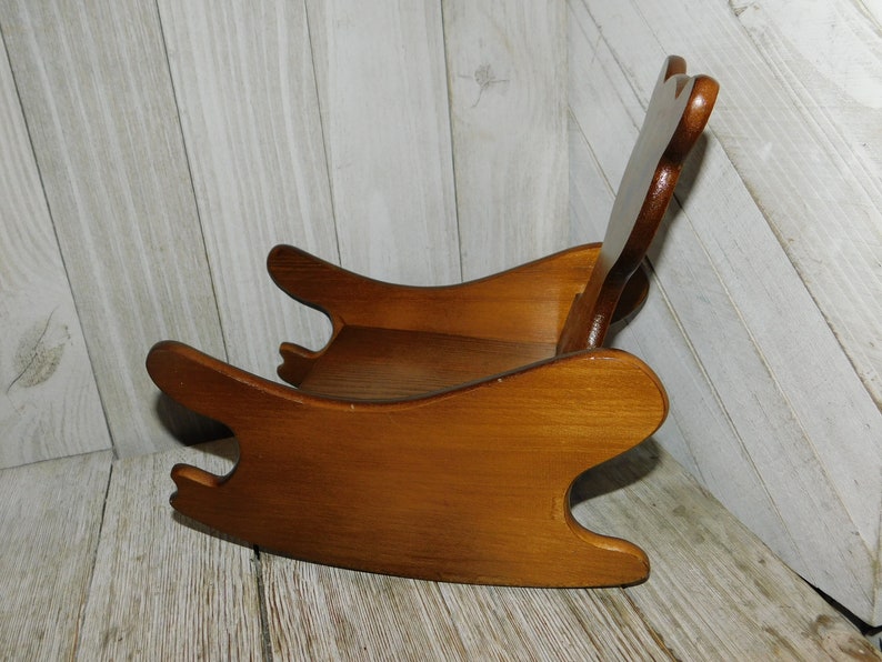 Puede incluir: Una silla mecedora de madera para ni&ntilde;os, con un acabado de tinte marr&oacute;n. La silla tiene un dise&ntilde;o sencillo con un respaldo redondeado y un asiento ancho.