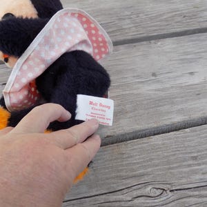 May include: A vintage Minnie Mouse plush toy with a black body, orange feet, and a pink and white polka dot bow. The tag reads "Walt Disney Characters". The plush is on a weathered wooden surface.