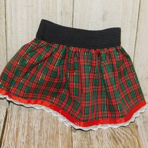 May include: A red, green, and gold plaid skirt with a black elastic waistband and white lace trim. The skirt has a red ribbon around the bottom.
