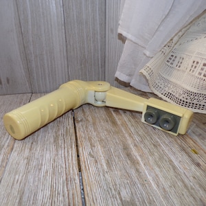 May include: A white plastic hand crank with a gray plastic handle and two gray plastic knobs. The crank is designed to be used with a window blind.