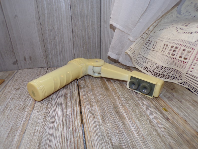 May include: A white plastic hand crank with a gray plastic handle and two gray plastic knobs. The crank is designed to be used with a window blind.