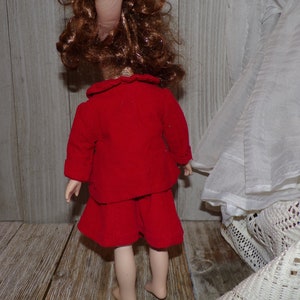 K&ouml;nnte beinhalten: Ein rotes Cordkleid mit wei&szlig;em Kragen und langen &Auml;rmeln. Das Kleid wird von einer Puppe mit braunen Haaren getragen.