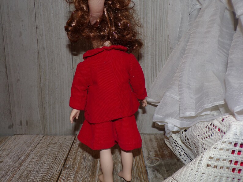 K&ouml;nnte beinhalten: Ein rotes Cordkleid mit wei&szlig;em Kragen und langen &Auml;rmeln. Das Kleid wird von einer Puppe mit braunen Haaren getragen.