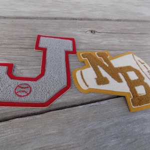 May include: Two felt patches, one shaped like a letter J with a baseball inside, the other shaped like a megaphone with the letters NB inside. The J patch is red and gray, the NB patch is yellow and white.