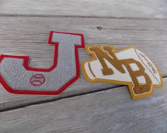May include: Two felt patches, one shaped like a letter J with a baseball inside, the other shaped like a megaphone with the letters NB inside. The J patch is red and gray, the NB patch is yellow and white.
