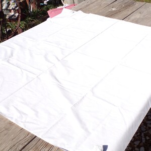 May include: A white cotton tablecloth with a smooth texture, folded and laid out on a wooden surface.
